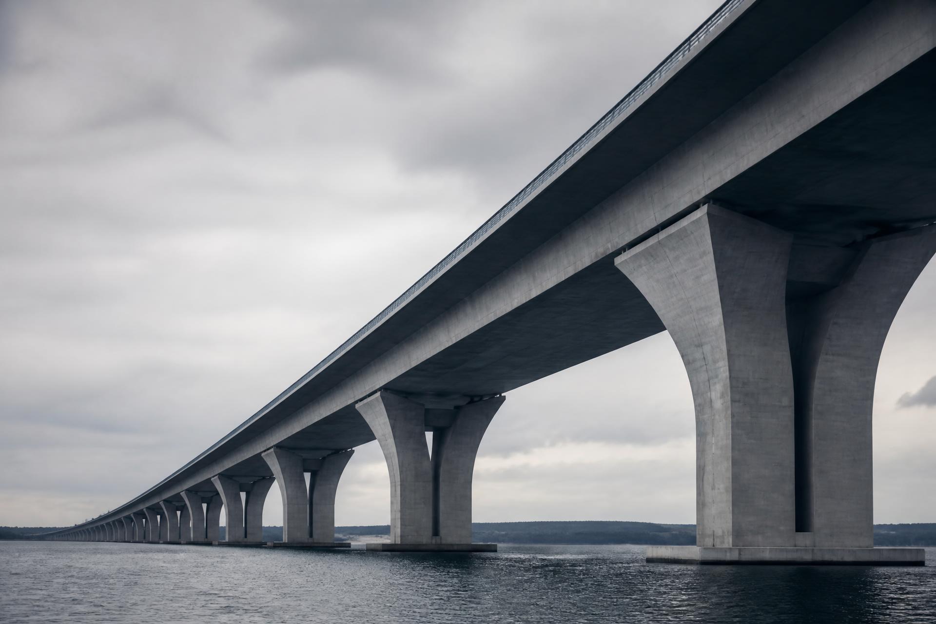 A long concrete viaduct extending across calm water under an overcast sky